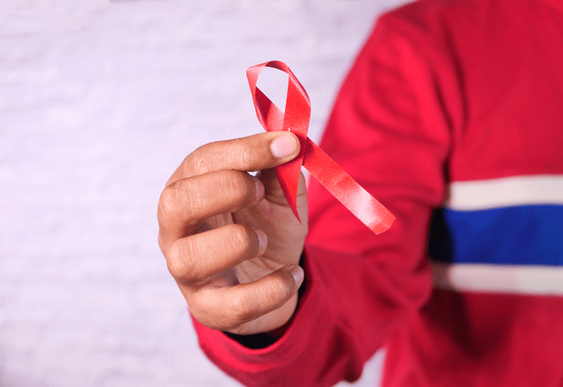person in a red shirt with blue and white stripe across the chest is holding a red awareness ribbon standing against a white background