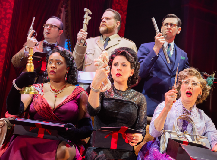 Three women in formal evening attire are seated on a 1950’s-style brown couch. Three men in suits stand directly behind them. Each person is holding a murder weapon up in the air, looking at it.