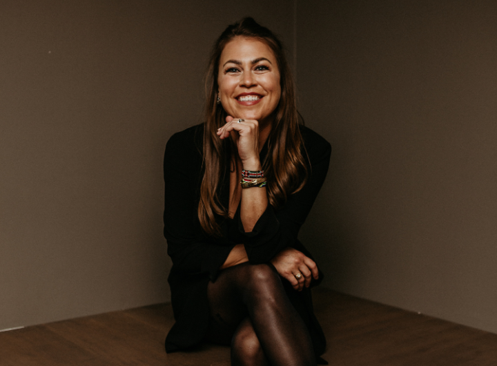 Person in a black outfit sitting with crossed legs and wearing bracelets.