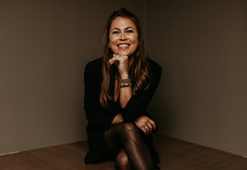 Person in a black outfit sitting with crossed legs and wearing bracelets.