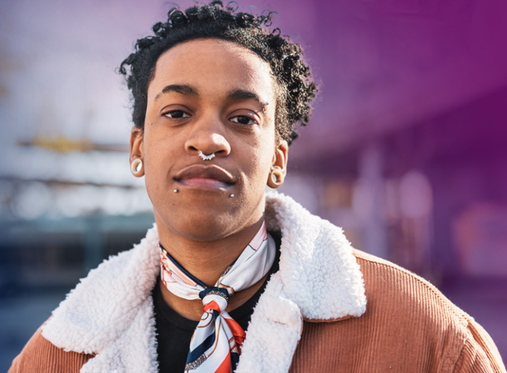 Person with curly hair, wearing a scarf, earring, and a textured jacket.