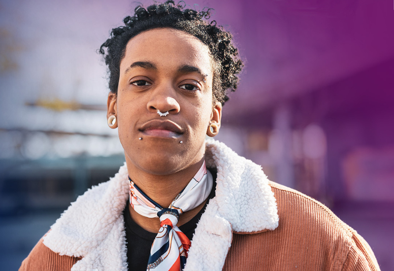 Person with curly hair, wearing a scarf, earring, and a textured jacket.