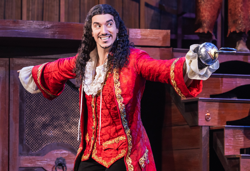 Person in a red period costume with a sword on a stage.