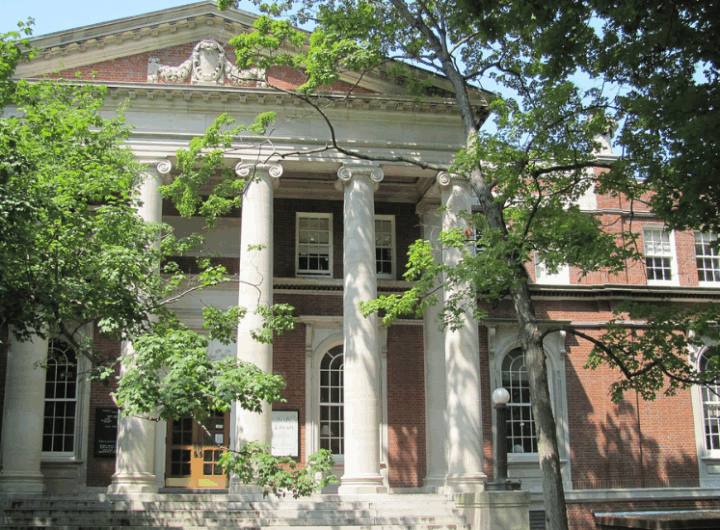 Historic library building with grand columns, brick facade, and surrounding greenery on a bright, sunny day.