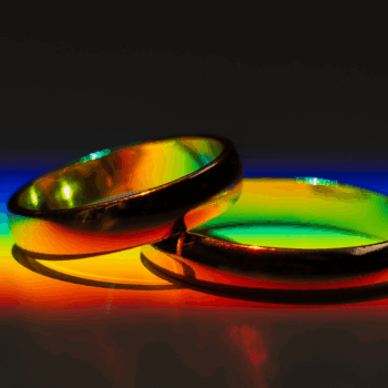 Two gold wedding rings resting on a vibrant rainbow spectrum, casting colorful reflections against a dark background.